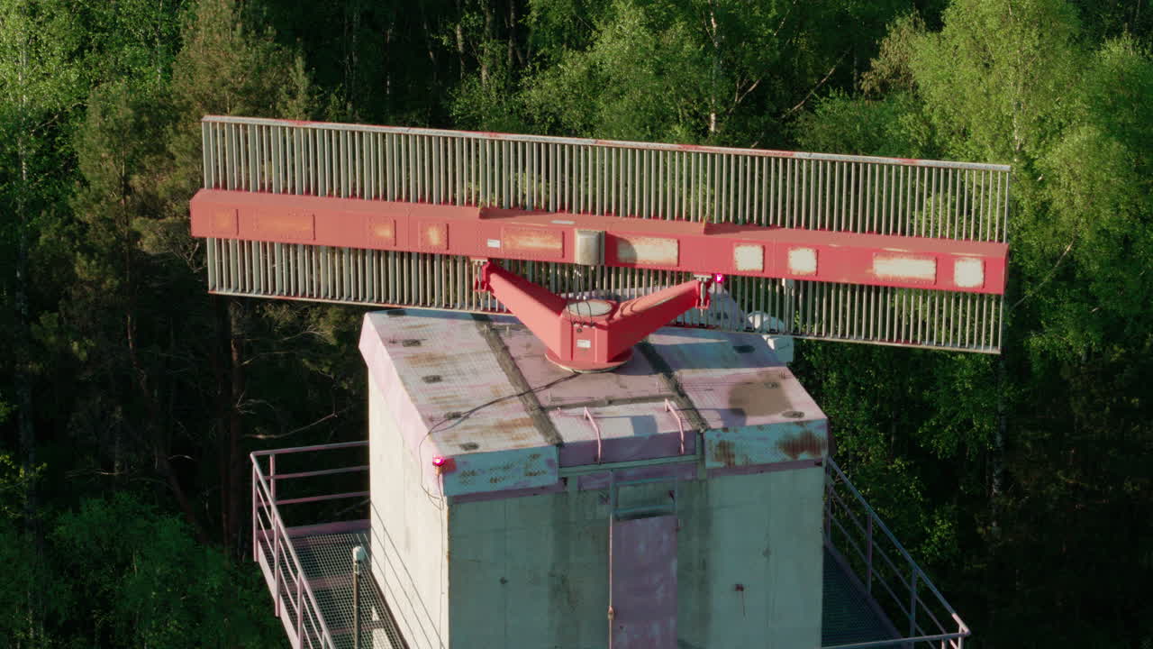 Old and worn secondary surveillance radar for air traffic control rotating in the middle of forest with city visible in background. Close-up shot.