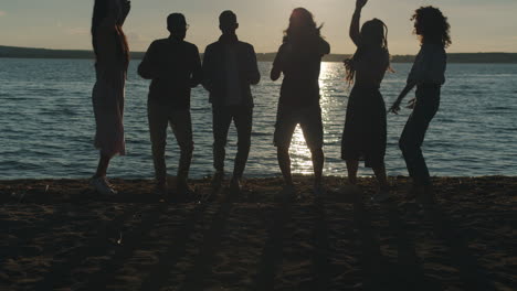 friends dancing on beach at sunset