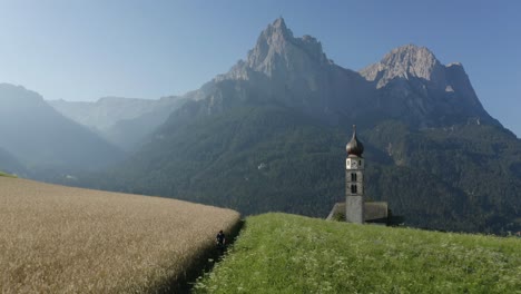 secluded nature grass and wheat field with a small church in europe mountain backdrop french alps, kastelruth, trentino