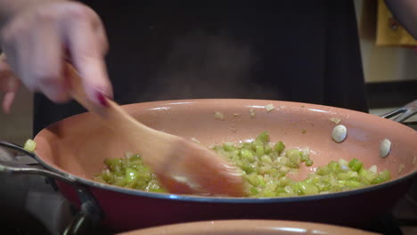 woman sautés onions and celery with wooden spoon for thanksgiving stuffing , close up -- 4k