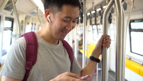 close up of young man listening to music with wireless earpods and using mobile phone while commuting by train. asian guy enjoying music on the go