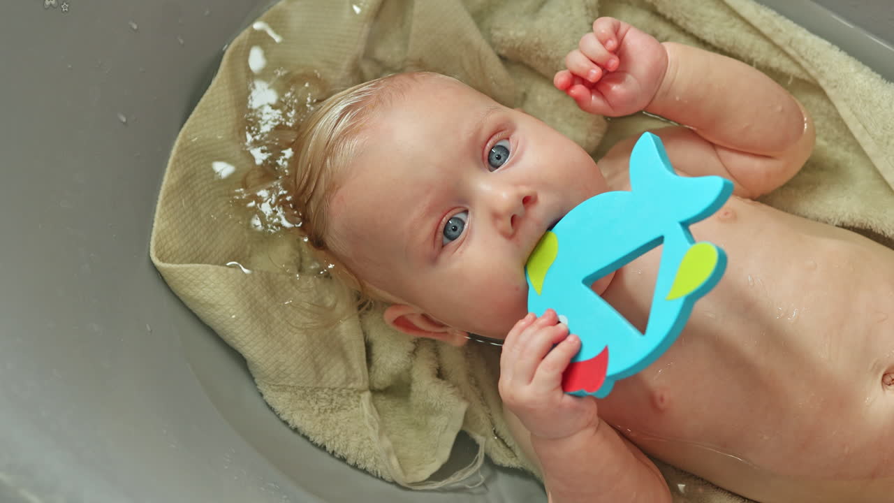 Bebé acostado en una bañera de plástico y bañándose. Bañando a un niño en agua clara. El niño yace en el agua.