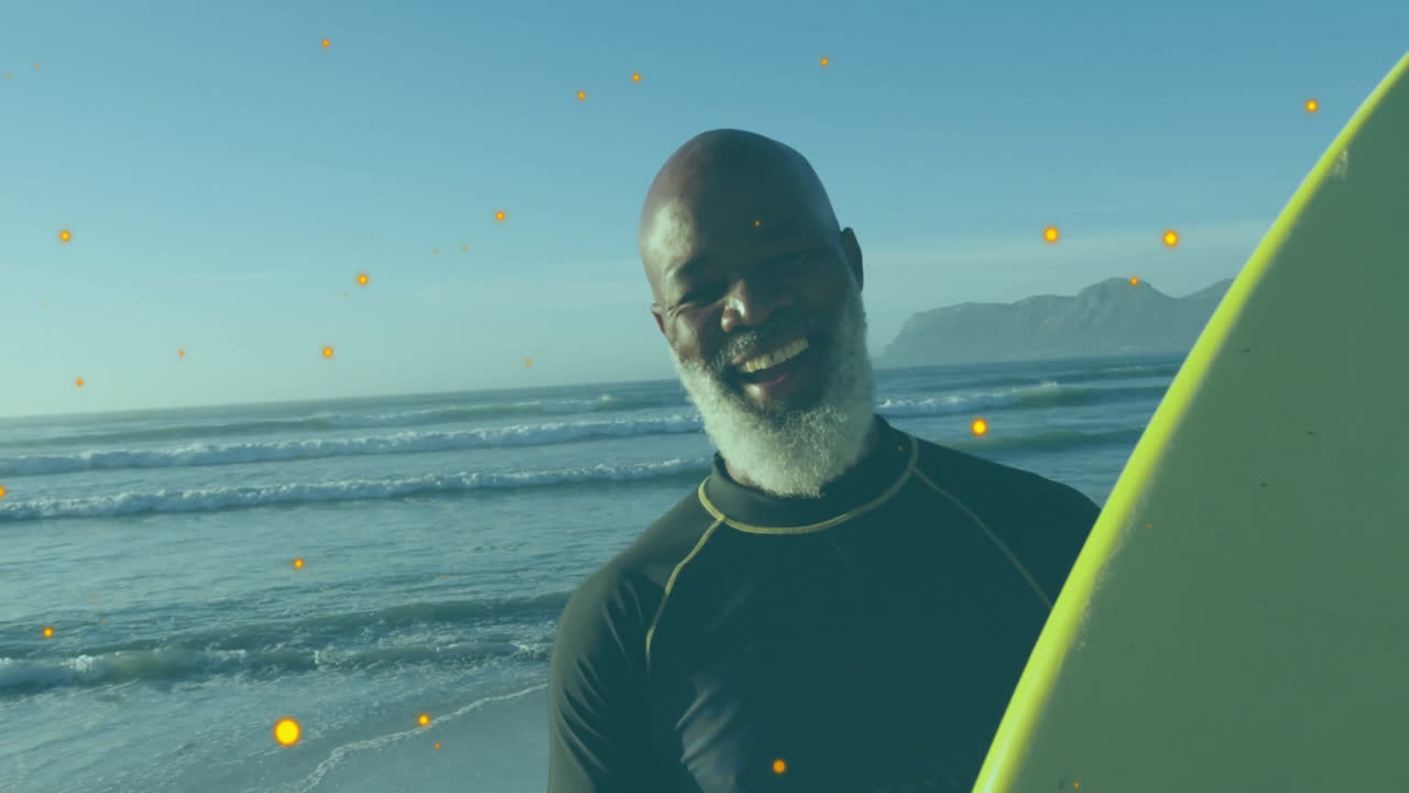 On beach, man with surfboard surrounded by glowing animation particles smiling