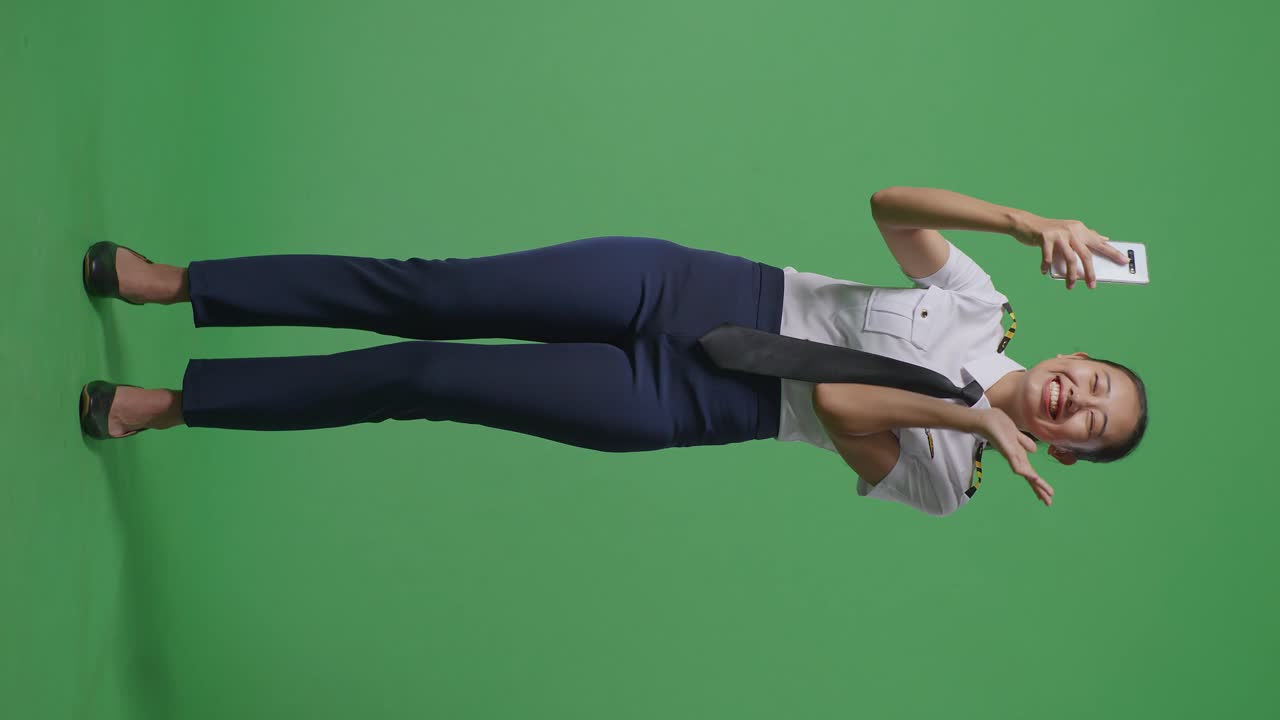 녹색 스크린 배경 스튜디오에 서서 사진을 찍는 스마트폰을 사용하는 아시아 여성 조종사의 전체 몸