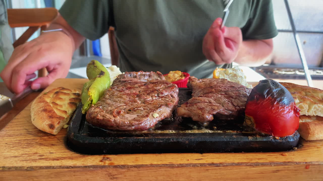 Close-up of sizzling meat, tomato, pepper, and bread on a hot stone plate in Istanbul, with a person cutting and eating the dish