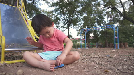 slider shot of an east asian boy kid focused having fun playing playing with a toy truck at a park in the forest