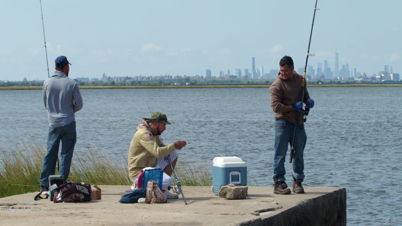Three Men Fishing in Queens, New York, on Clear Day with Manhattan Skyline in Distance