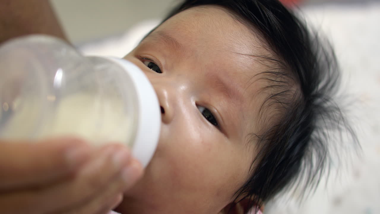 A nurturing mother feeds her baby girl with a bottle, emphasizing the care and nourishment crucial for her baby’s healthy development and physical growth.