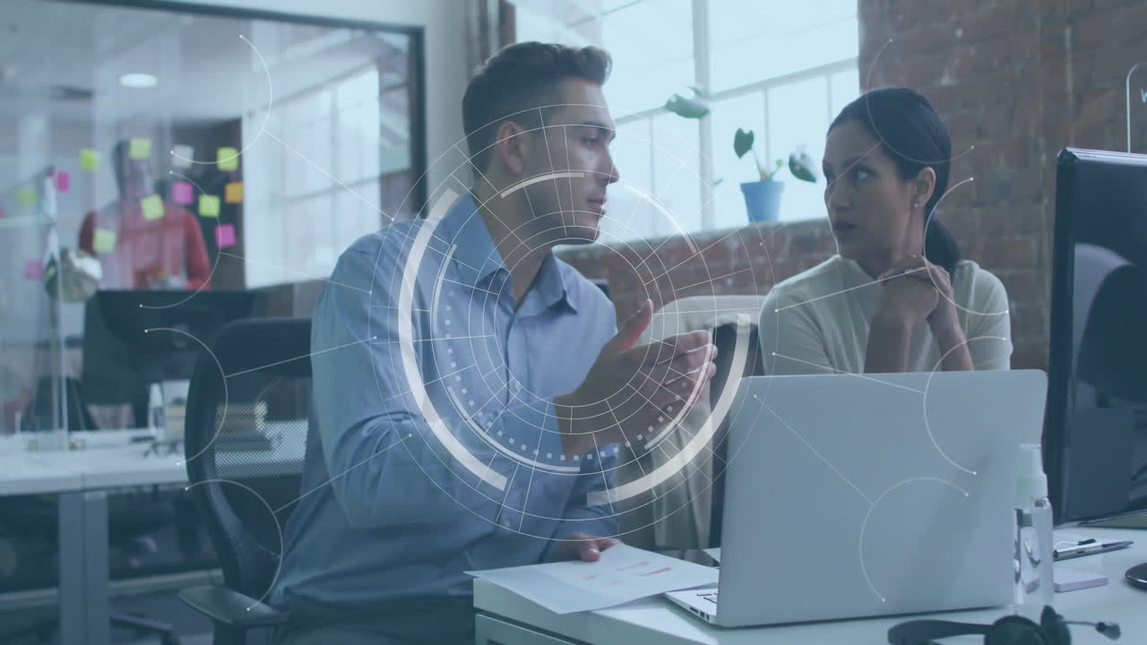 Male coworker gesturing while female coworker listening in business office, showing floating charts
