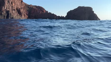 Tilt-up-from-sea-surface-to-cliffs-of-Scandola-peninsula-nature-reserve-in-summer-season-as-seen-from-moving-boat,-Corsica-island-in-France