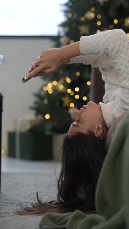 woman relaxing by christmas tree with phone