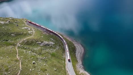 aerial clip showing a train moving along the green hills adjutant to a lake with blue water