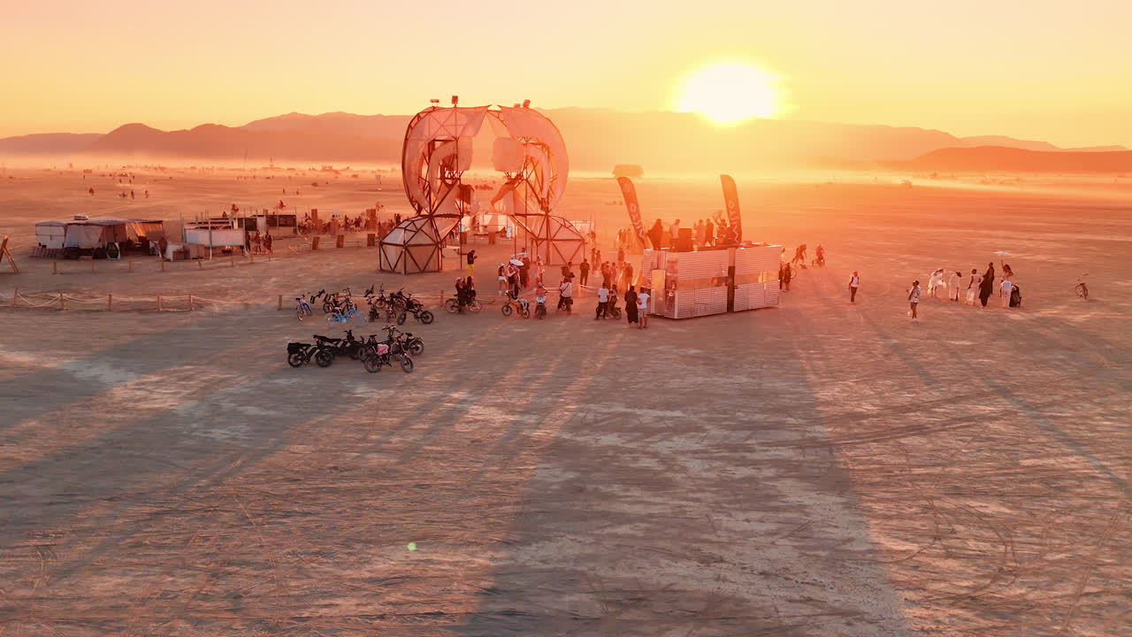 Nevada, USA, 14 August 2025: Sunset view of Burning Man art installation and festival crowd in Nevada desert.. The sun sets behind an art installation and festival crowd. Long shadows stretch across the playa in Nevada desert