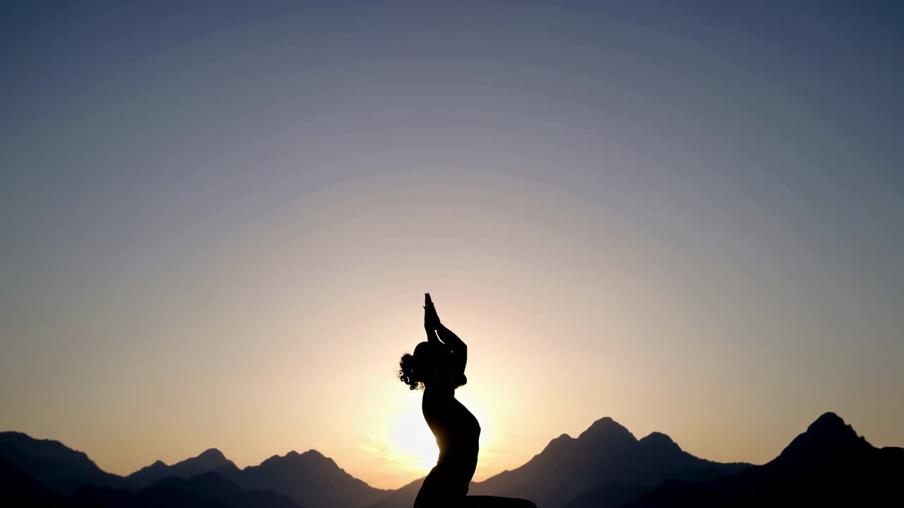 Silhouette di una persona in posizione yoga all'alba, con montagne sullo sfondo