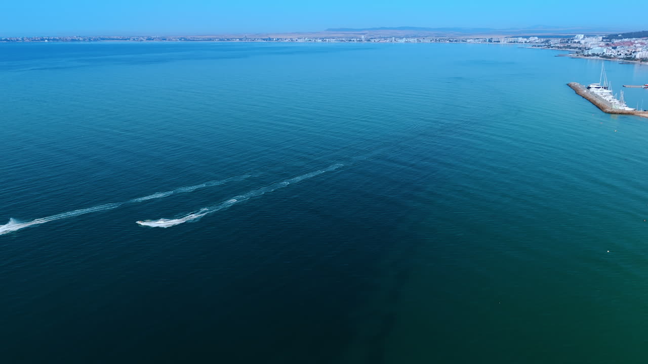 Boats glide on calm beach seas. Two boats race through tranquil waters near a coastline, showcasing a bright blue sky and distant shoreline scenery