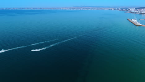 boats glide on calm beach seas. two boats race through tranquil waters near a coastline, showcasing a bright blue sky and distant shoreline scenery