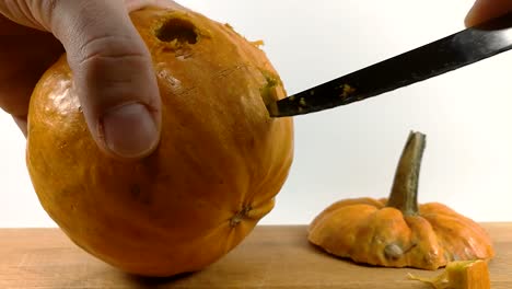 carving pumpkin part 4, person carving teeth into halloween pumpkin with a small pointy serrated knife on wooden chopping board, still, isolated, slomo