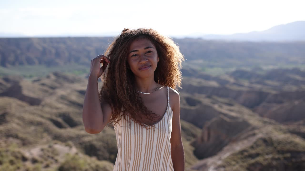 Young woman with curly hair posing in a sunny desert landscape