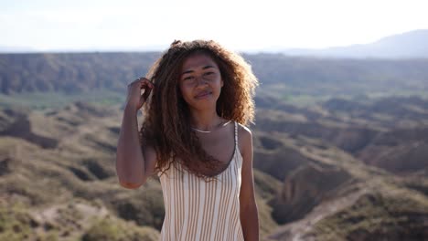 young woman with curly hair posing in a sunny desert landscape