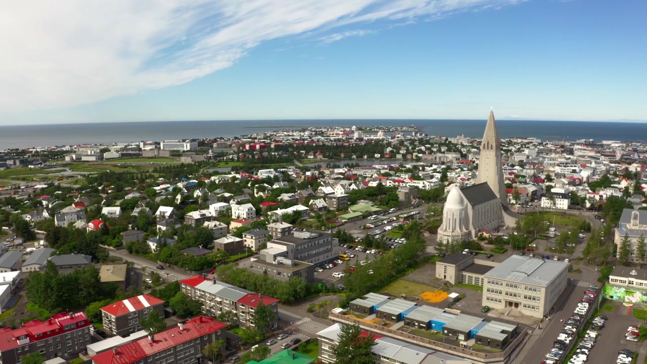 Ripresa aerea con drone che sorvola la città di Reykjavik, Islanda, in una giornata di sole. La vista mostra l'iconica chiesa di Hallgrímskirkja e lo skyline colorato della città con l'oceano sullo sfondo