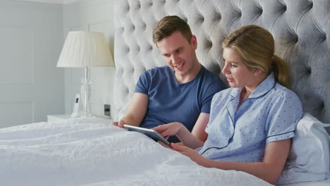 couple at home in bed self isolating using digital tablet during covid 19 lockdown