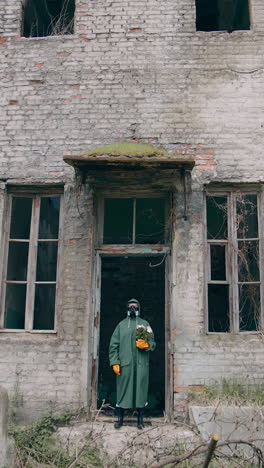 Person in safety uniform alone in radiation zone. Man in protective suit and gas mask with flowers near abandoned building after the chemical attack. Vertical video