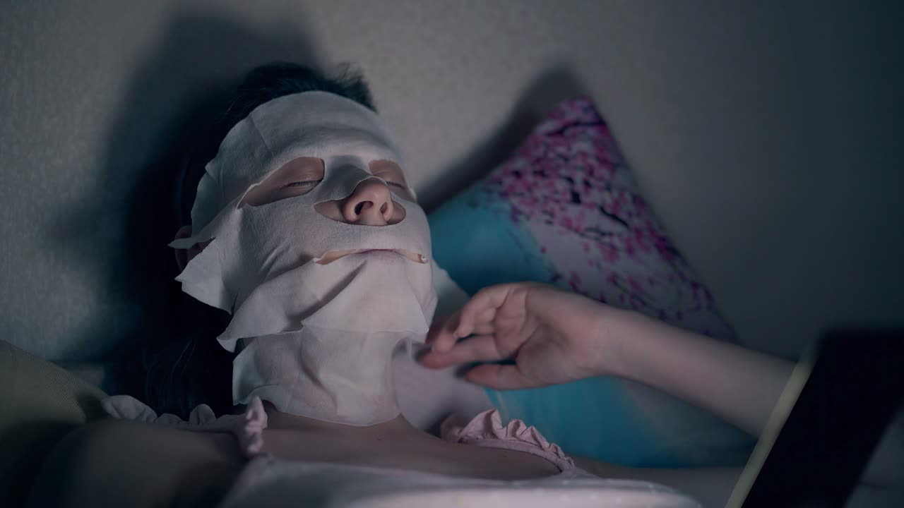 얼굴에 시트 마스크를 쓴 젊은 여성이 베개에 누워 있습니다.