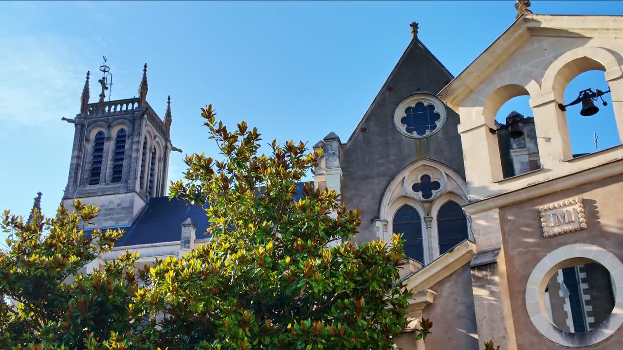Architectural details of historic Saint-Pierre church in Changé, Mayenne, bell tower and facade against clear blue sky on sunny day, France. Panning