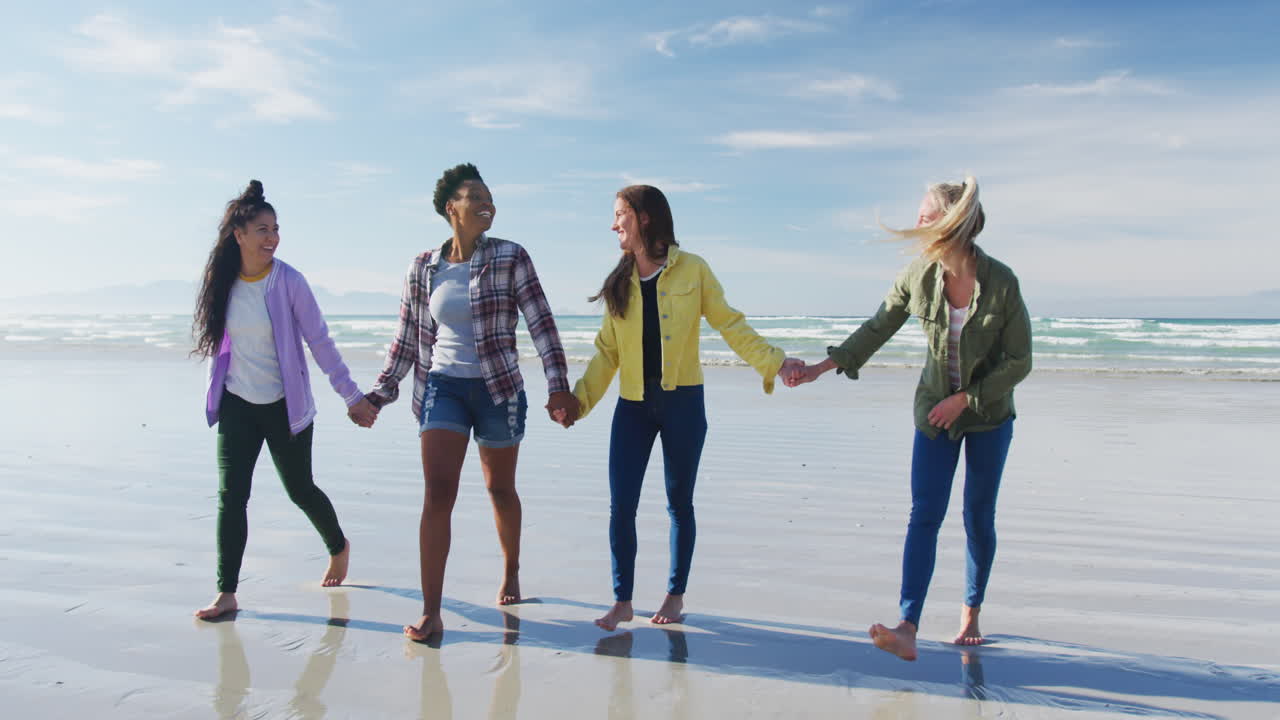 다양한 여성 친구들의 행복한 그룹이 손을 잡고 해변을 고 재미를 느끼고 있습니다.