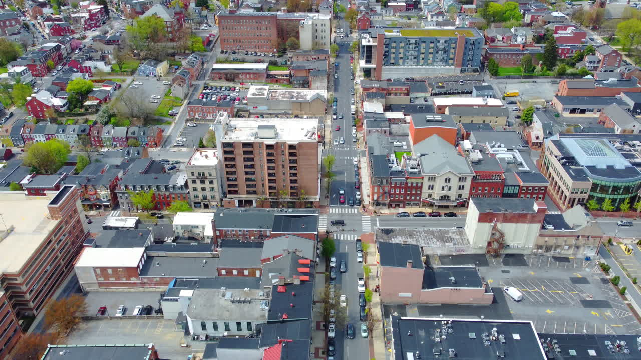 A drone glides directly above a main street in Lancaster City, PA, revealing a geometric grid of rooftops, crosswalks, traffic, and architecture—showcasing the vibrant rhythm of small-city life.