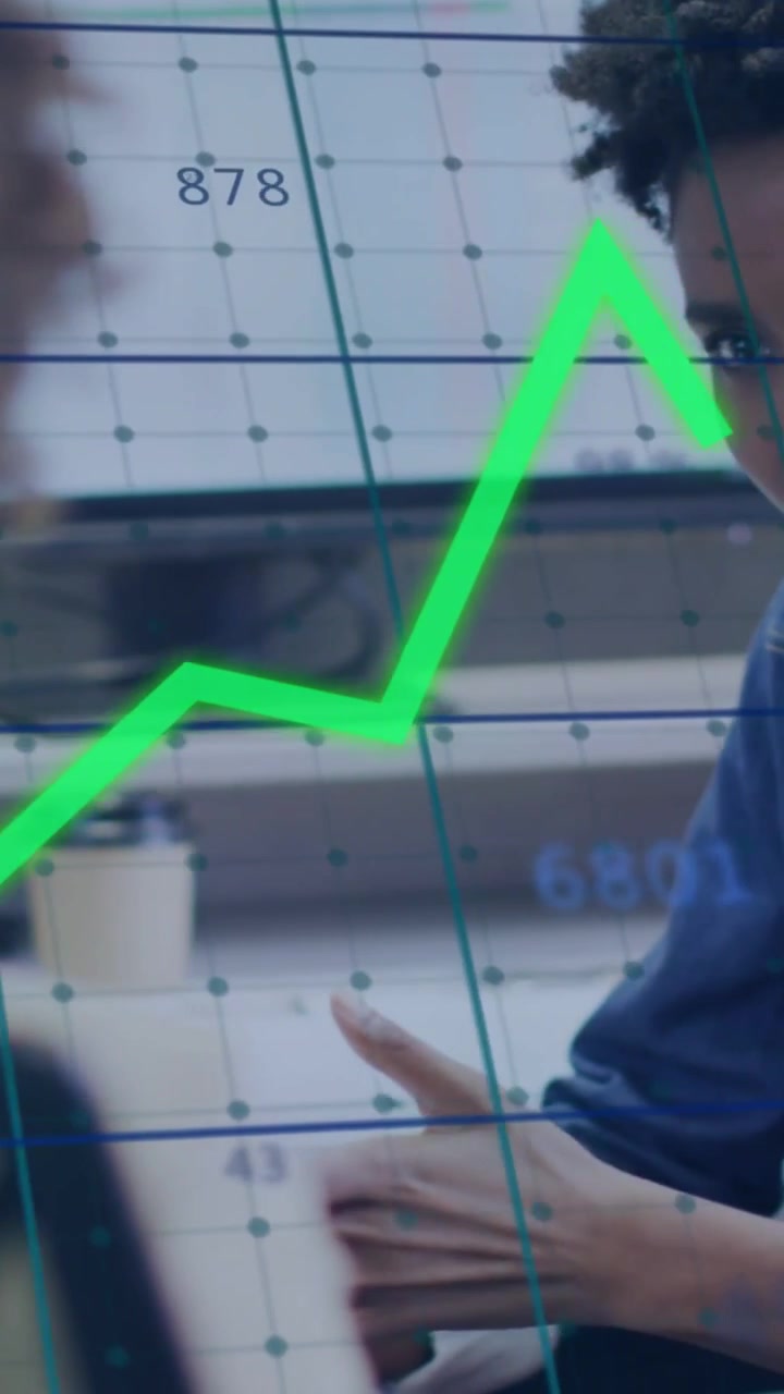 Video verticale: Donna a destra che guarda un grafico finanziario in tempo reale con percentuali, dopo che un collega ha mostrato il laptop per una revisione.