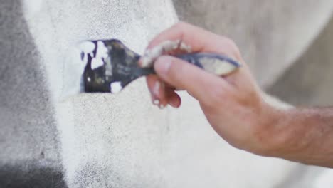 video de la mano de un artista masculino caucásico pintando un mural en la pared usando pincel y pintura blanca
