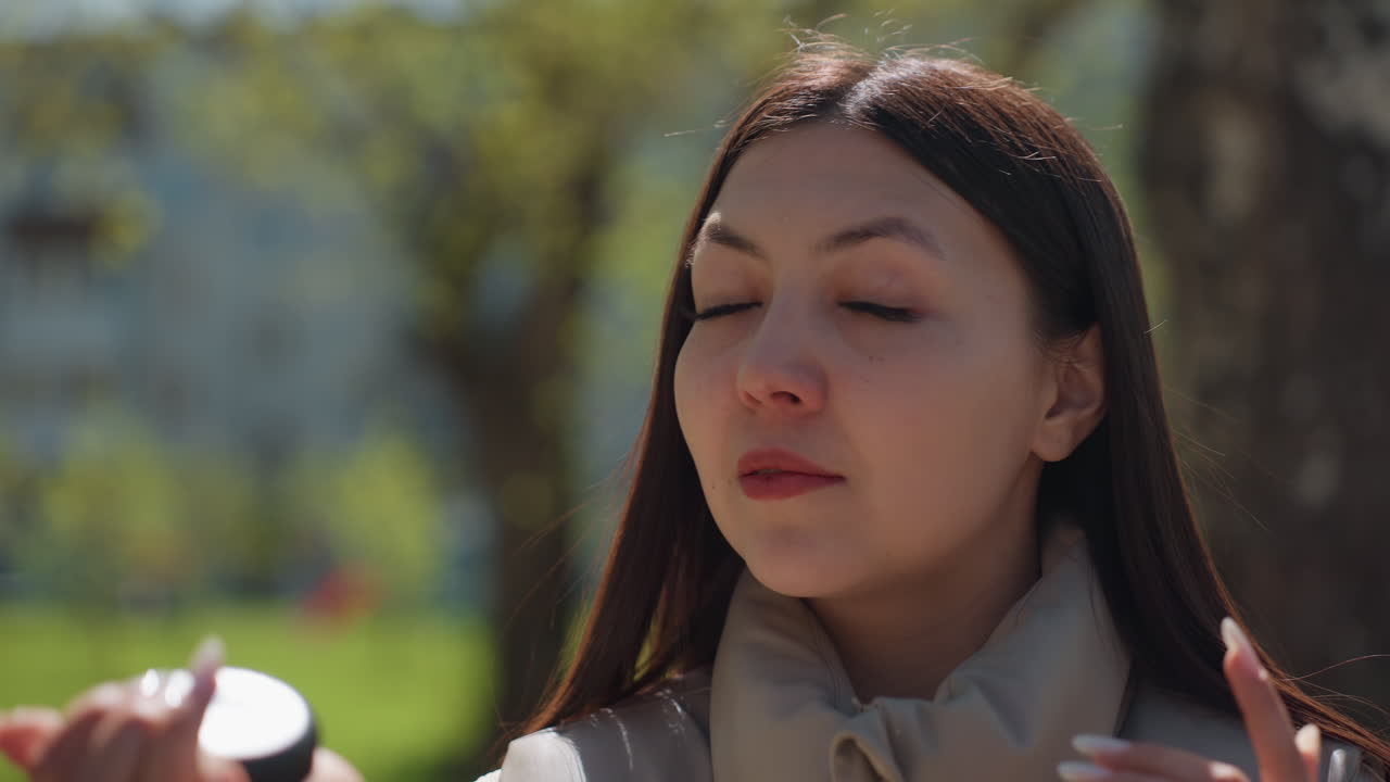 여성이 야외에서 우아하게 자신을 꾸미고 있어요. 여성이 휴대용 거울을 사용하여 야외에서 외모를 돋보이게 하고, 자연광으로 여성이 조심스럽게 화장하는 야외 장면을 보여줍니다.