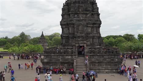 indonesia,prambanan temple on a cloudy day,greenery is shinning behind the temples,camera moves horizontally from left to right slowly,people walking around the temple complex in colorful cloths