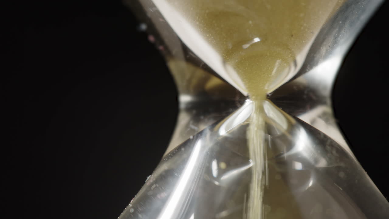 Extreme closeup of yellow grains of sand flowing through an hourglass