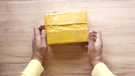 hands holding a yellow taped package on a wooden table