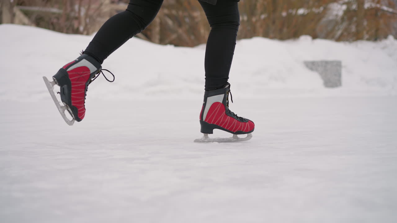Athletic leg in red skates striding on frozen outdoor rink in winter snow, showing motion, balance, coordination, and energy during recreational ice skating activity in cold seasonal environment