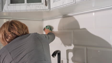 close up back view of woman wiping kitchen tiles with green cloth in modern clean bright home interior showing daily cleaning routine focus on cleanliness