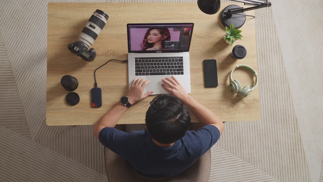 Top View Of Asian Male Editor Thinking About The Idea While Sitting In The Workspace Using A Laptop Next To The Camera Editing Photo Of A Female At Home