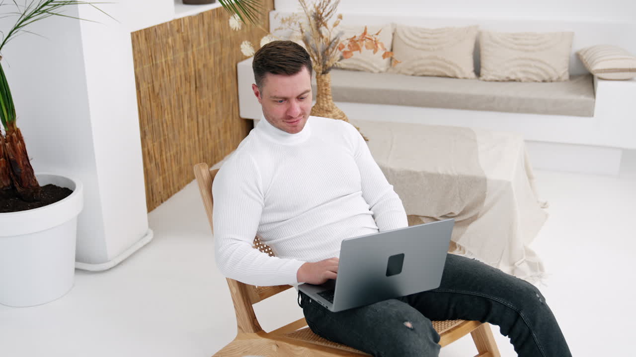 Hard-working male entrepreneur working on laptop sitting in armchair. Man closes his gadget, leans back in the armchair relaxing finally. Top view.
