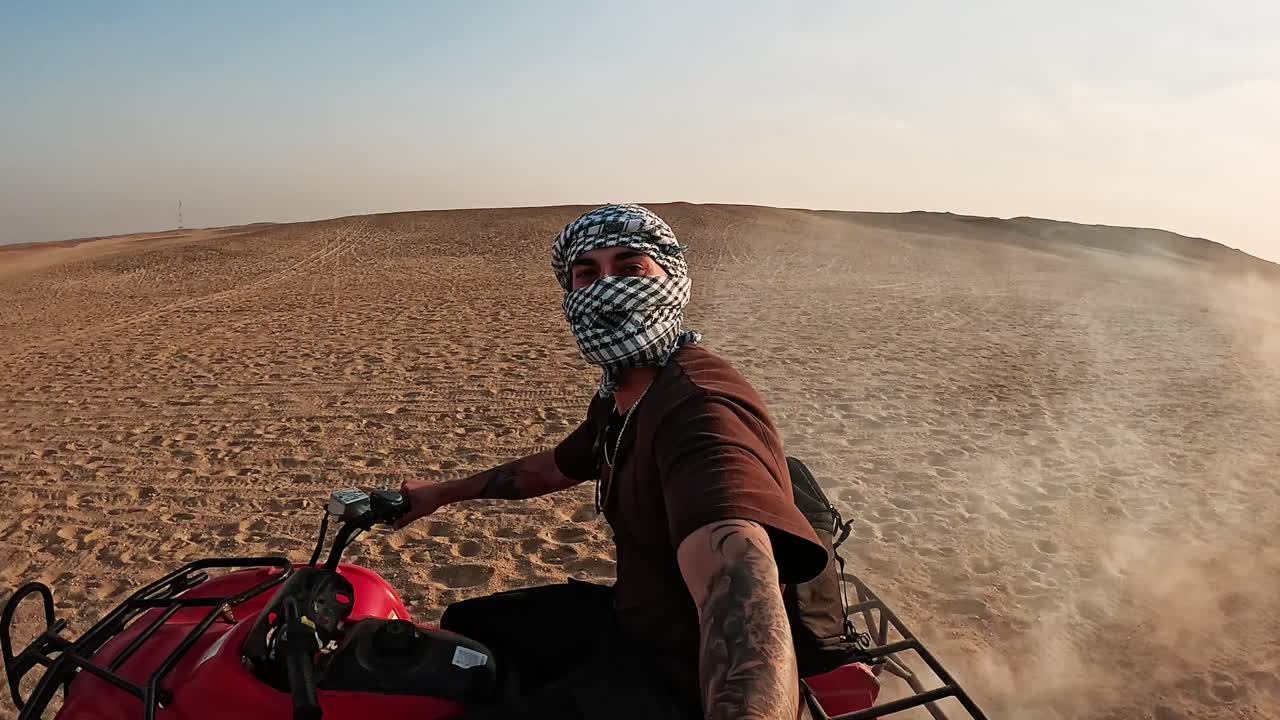 Uomo che guida un quad tra le dune del deserto al tramonto