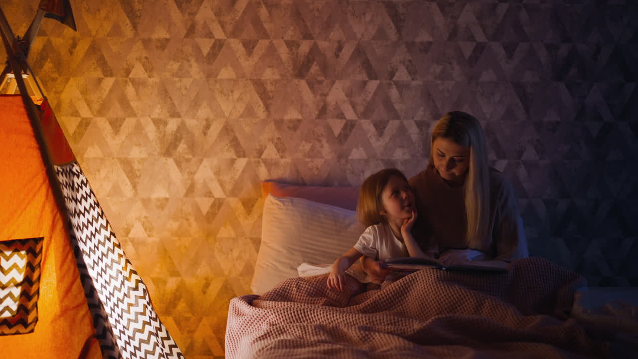 Cute little girl yawns and mother embraces kid in bedroom