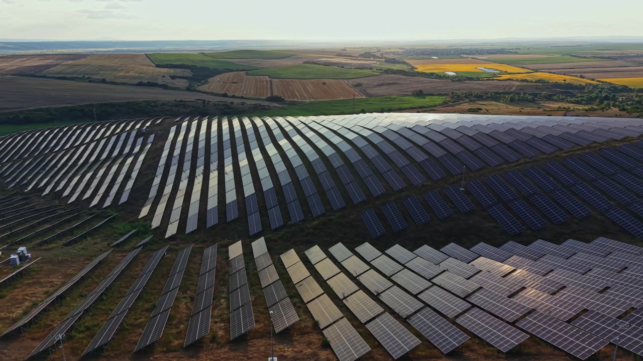 Solpaneler dækker et stort område på en mark nær landbrugsjord og opfanger sollys til energi på eftermiddagshimlen.