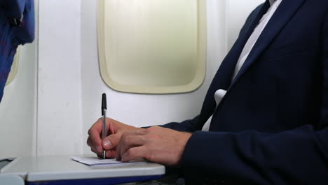 Unrecognizable-business-man-writing-on-immigration-form-on-an-airliner-plane