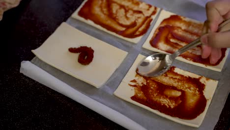 disparo en primer plano de la mano poniendo pasta de tomate en la masa de pizza cuadrada pequeña