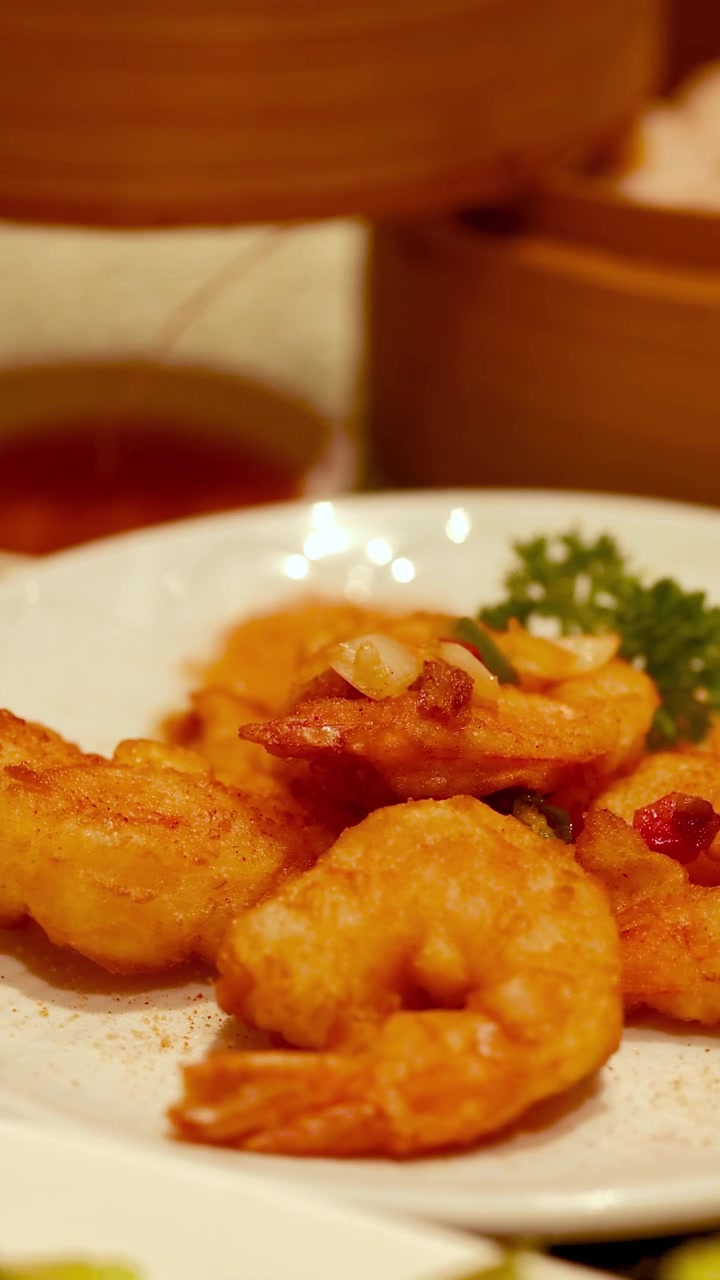Camarão dourado frito servido com molhos num ambiente de restaurante chinês acolhedor e convidativo.