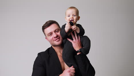 loving father holding a little baby on his shoulder. happy little child pushes the pacifier to his mouth. studio footage. white backdrop.