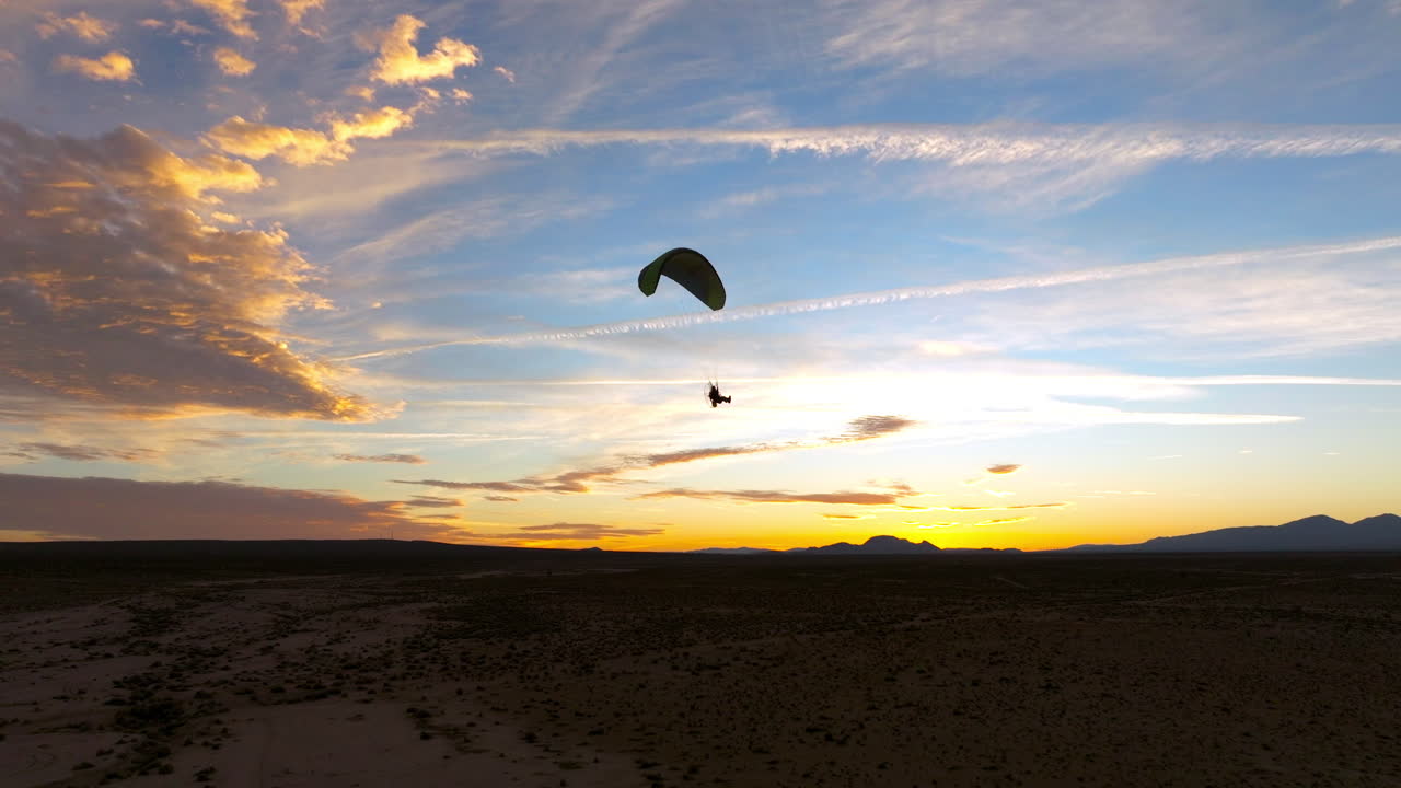 silueta de un parapente motorizado que vuela sobre el desierto de mojave durante una colorida puesta de sol