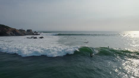 Toma-Aérea-De-Carro-Hacia-Atrás-De-Surfistas-Esperando-Y-Atrapando-Olas