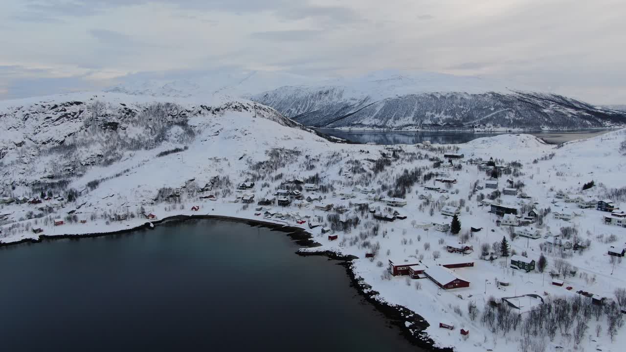 Drone view in Tromso area in winter flying over a fjord towards a small snowy town with small houses in Norway